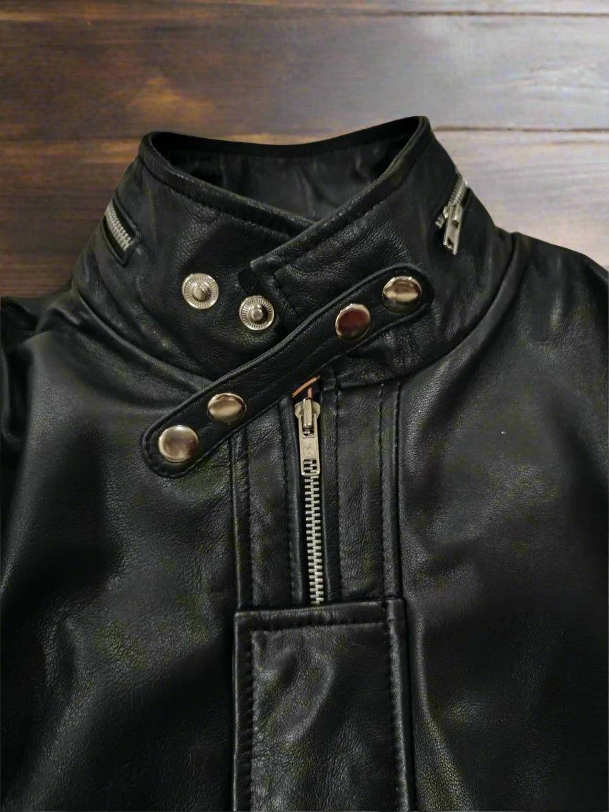 Close-up of a black leather jacket with silver buttons and zippers on a textured surface.
