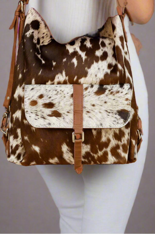 Brown and white cow print bag with a flap over pocket on a plain background