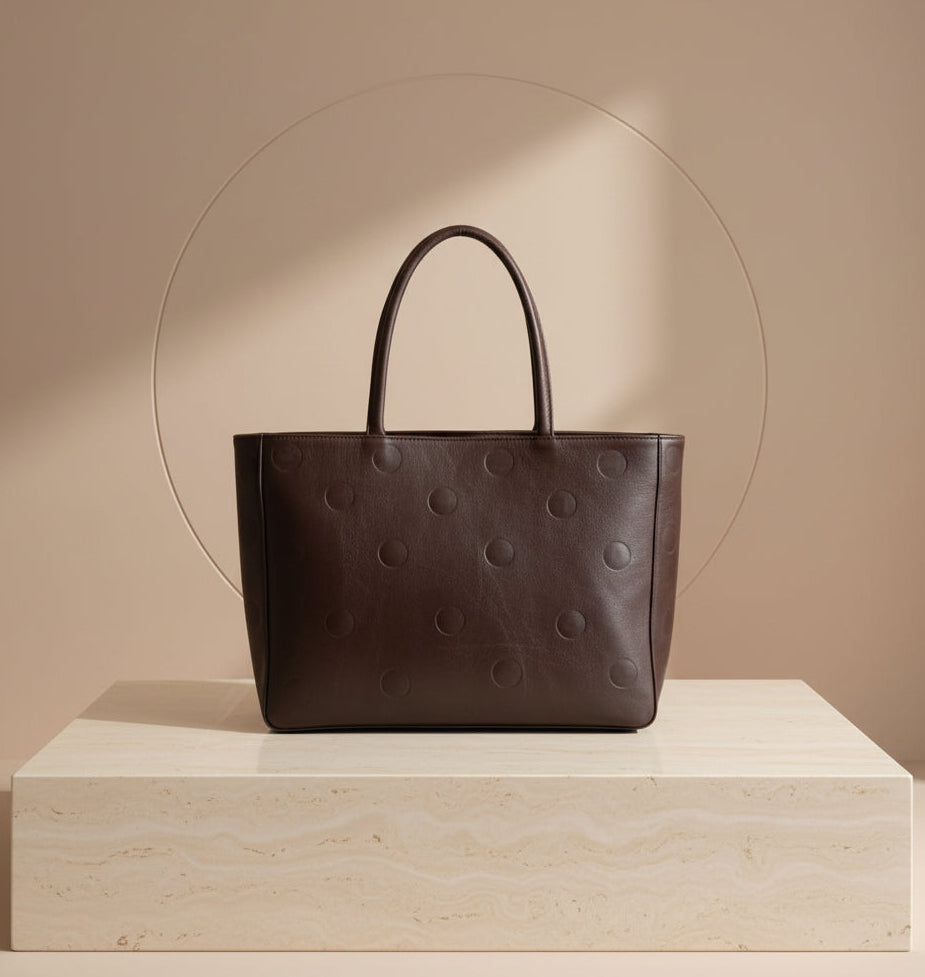 Brown leather tote bag with circular patterns on a wooden surface