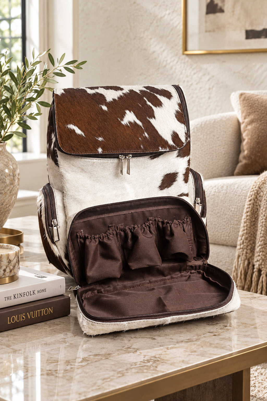 a brown cowhide diaper backpack kept on a table against a window 