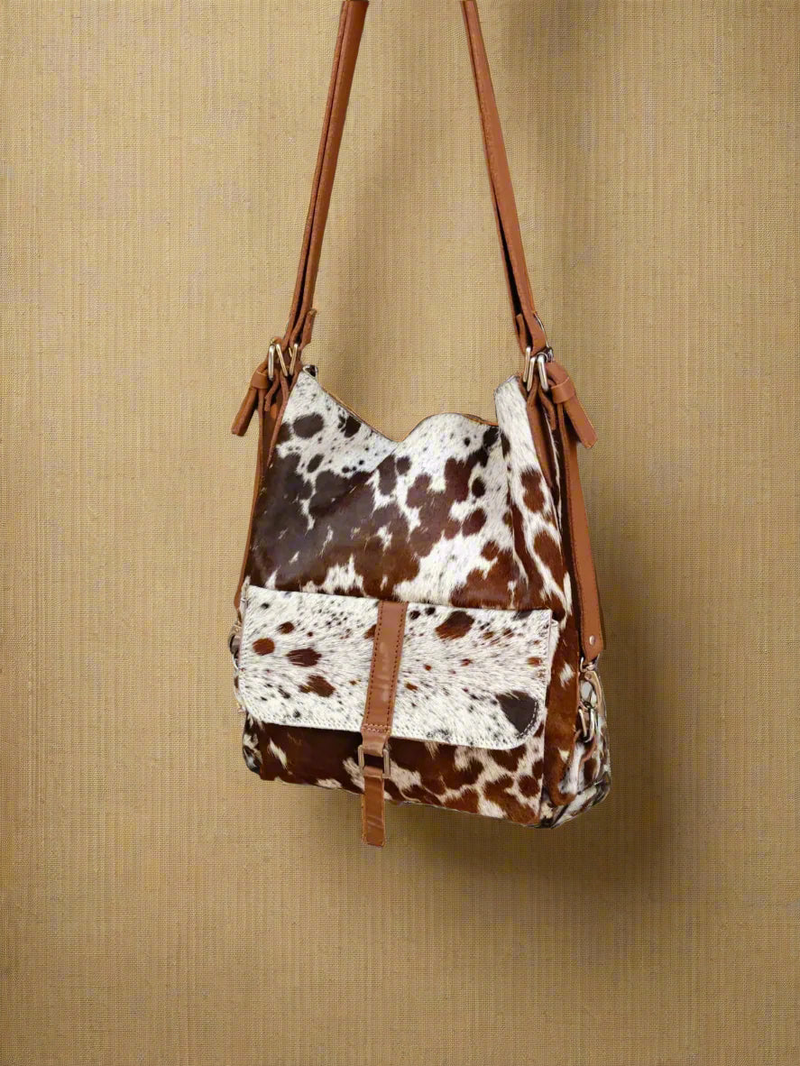 Cow print handbag with brown leather straps on a beige background
